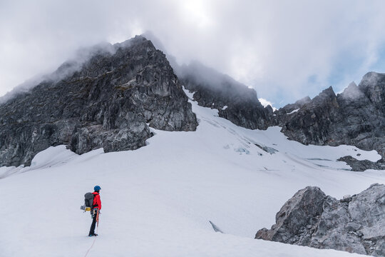 One Mountaineer Standing on Glacier Looking at Rocky Mountain Peak