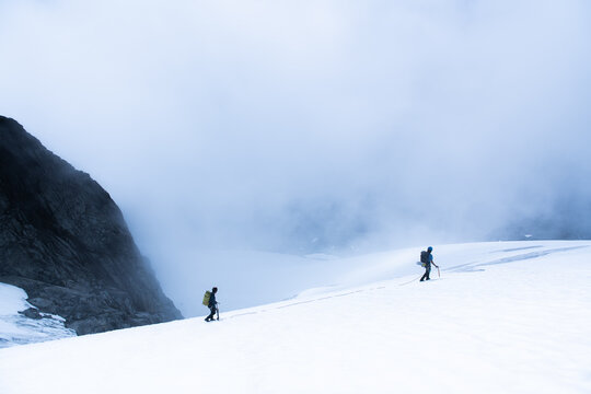 Two Climbers Traversing Snowy Glacier in Foggy Mountain Landscape