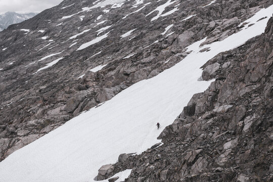Solo mountaineer crossing a snowfield on a vast rocky slope