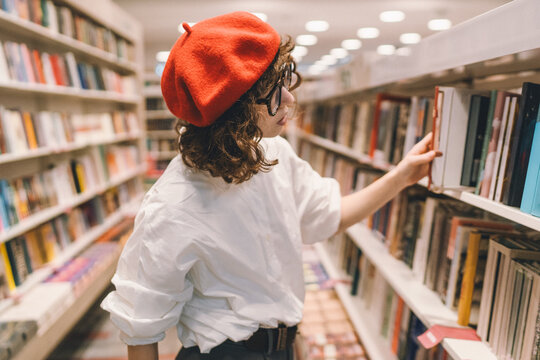 Young student woman in red beret choosing book in library