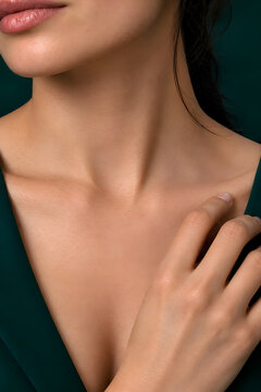 Close up of elegant woman with hand on collarbone and glowing neck against dark green background for jewelry necklace and ring mockup display template