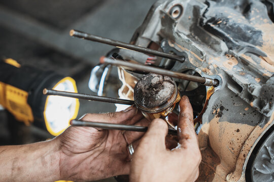 Mechanic hands installing a piston into a motorcycle engine block during repair and overhaul in a garage workshop.