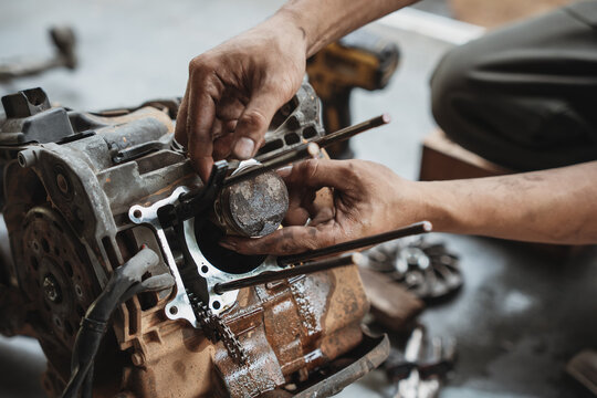 Mechanic hands installing a piston into a motorcycle engine block during repair and overhaul in a garage workshop.