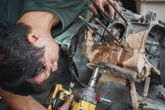 Mechanic using an electric impact wrench to repair a motorcycle engine in a garage workshop.