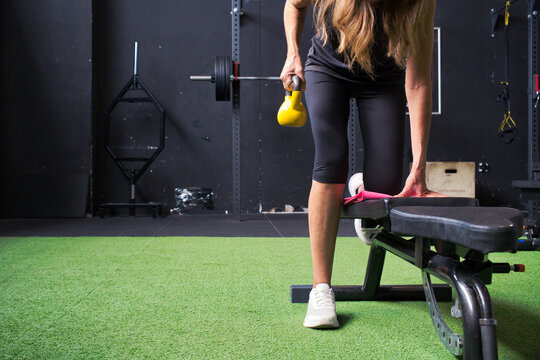 Mature woman doing a one-arm kettlebell row on a bench in a functional training gym, strength workout for healthy aging and fitness