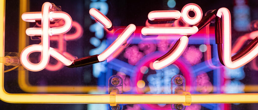 Close-up of glowing white Japanese hiragana characters on a vibrant pink and blue neon light sign against a dark background