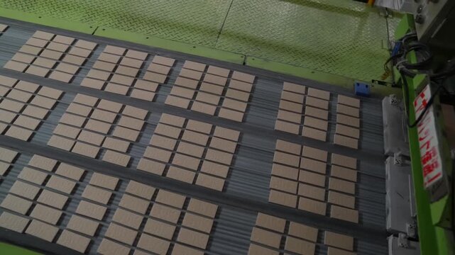 Automatic transfer press lifts above a wide bed of tan pressed tiles on a green production machine