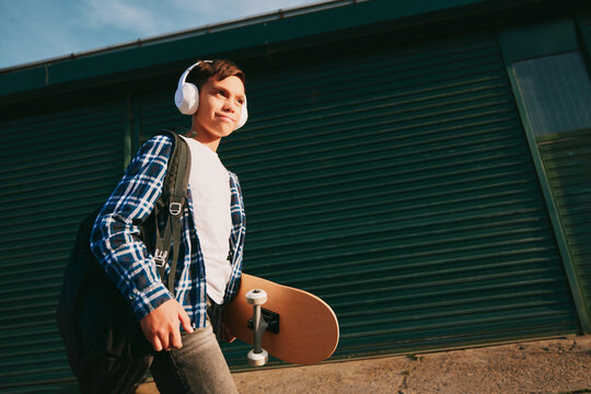 Boy carrying skateboard and backpack while walking outdoors