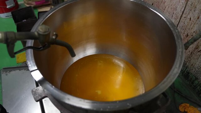 Golden orange liquid binder swirling inside a large stainless steel mixing bowl mounted on a paint mixer