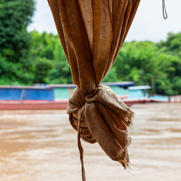 A brown curtain tied back reveals the muddy Mekong River and boats near Luang Prabang, Laos.