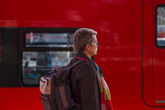 Person waiting at a train station beside a red train in the
