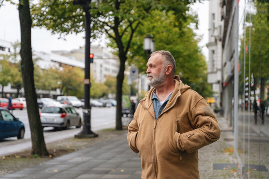 Man stands on city sidewalk with greenery and traffic in background