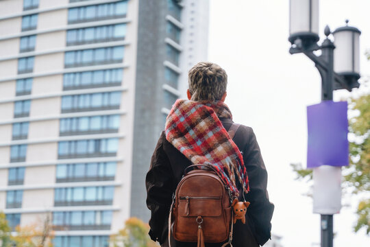 Person with backpack stands on city street near tall building