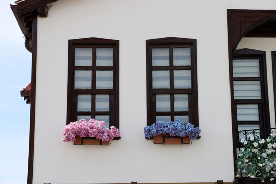 There are colorful flowers in front of small wooden windows. A view of architectural details from a Turkish house.