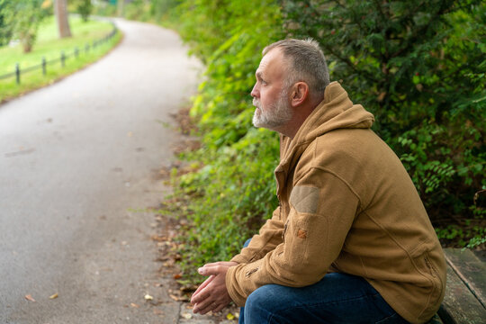 Man sitting on bench in a park on a quiet path surrounded by greenery