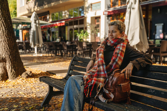 Woman sitting on a bench in a street cafe during autumn afternoon