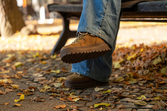 Footwear resting on a bench in area covered with autumn leaves in park
