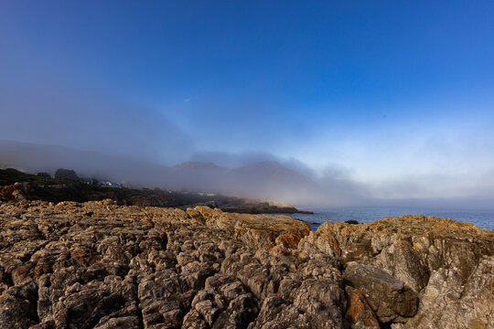 fog bank and afternoon sunlight over rocky coastline of Hermanus, South Africa