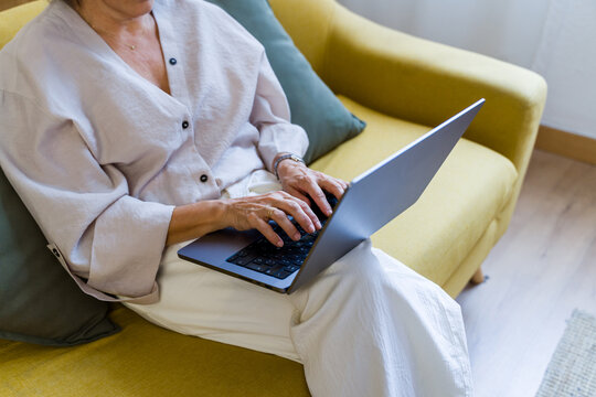 White woman typing on laptop on yellow couch indoors