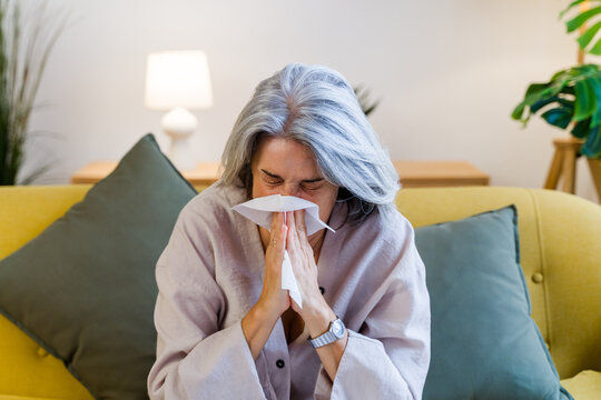 White woman sneezing into tissue on couch in living room