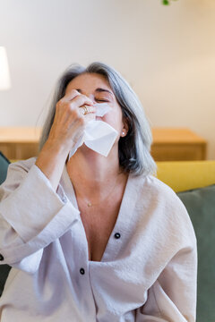 White woman blowing nose indoors in living room setting