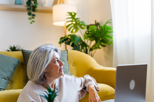 White woman sitting on floor by yellow sofa and laptop