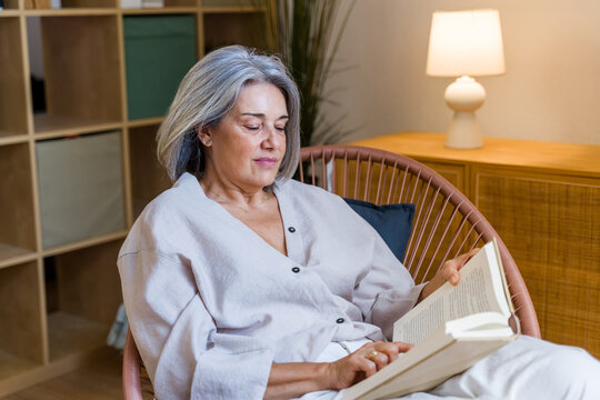 White woman reading book relaxing in chair indoors