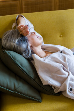 White woman relaxing on yellow sofa with green cushions indoors