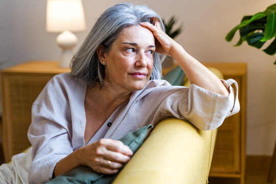 Middle-aged white woman sitting thoughtfully on yellow couch indoors