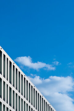 Modern office building with vertical facade lines beneath blue sky and clouds creating a minimal view of the modern office building and facade