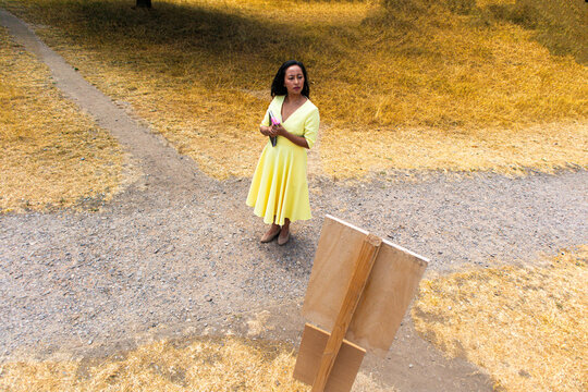 A woman in a yellow dress stands at a crossroads in a field