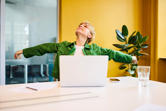 A businesswoman stretches her arms at her office desk