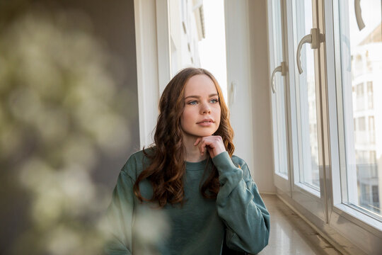 Teenage girl looking out of window, daydreaming