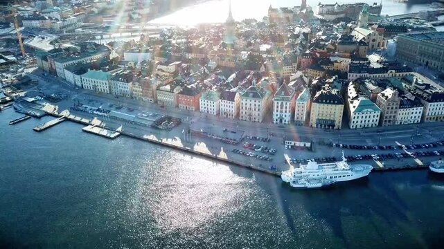 Rows of colorfully painted historic buildings on the edge of calm waters, complete with ships and boats docked at the docks and sparkling sunlight reflecting beautifully on the surface of the water.