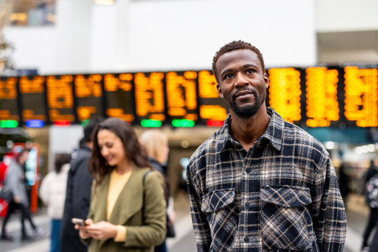 Man standing in city station in front of departure board