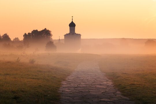 Silhouette of ancient Russian Orthodox church above misty field backlit by rising sun, Russia
