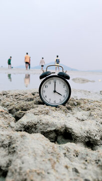 Vertical Alarm Clock at Four O'Clock on Seashore Rock for Time C