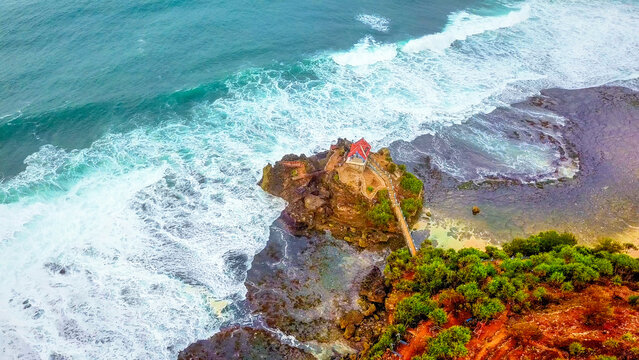 Aerial view of Kukup Beach Nature Inn featuring sandy beach, turquoise ocean waves, lush green coastal vegetation, and rocky cliffs in Kecamatan Tanjungsari, Daerah Istimewa Yogya, Indonesia.