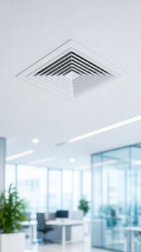Modern office interior with a focus on a white ceiling air vent and a bright workspace featuring desks, chairs, plants, and large windows.