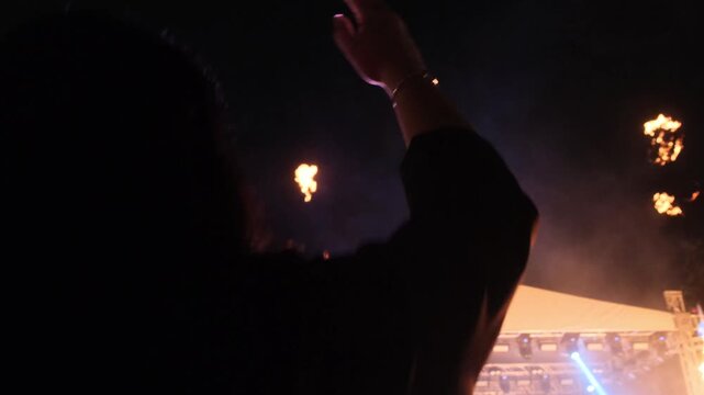 Young woman dancing at a nighttime concert with fire and light bursts, waving her hand and jumping to DJ music, escaping everyday stress and recharging with energy, emotional release