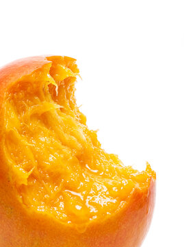 Close-up of ripe mango with bitten section, juicy orange flesh exposed on white background