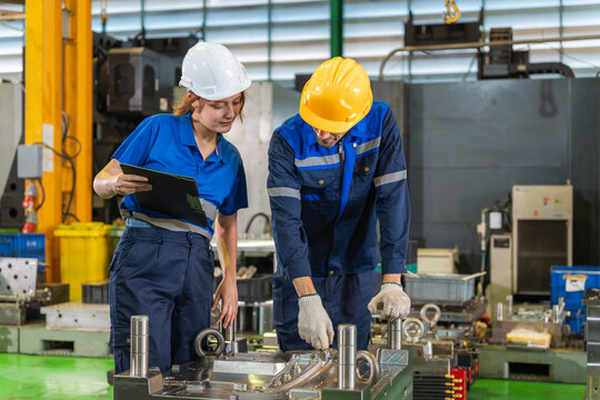 Diverse team of industrial engineers inspecting machinery and production quality in plant, professional factory workers wearing safety helmets reviewing work on clipboard in workshop