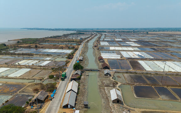 Aerial view of Salt Ponds in Kedung, showing rectangular salt evaporation pans, a narrow canal, small wooden huts, and a road running alongside the coast in Kedung, Central Java, Indonesia.