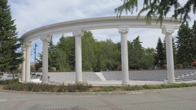 A semicircular colonnade of white Ionic columns above open air amphitheater seating at Odeon Square, in the lakeside town of Pogradec, southeast Albania.