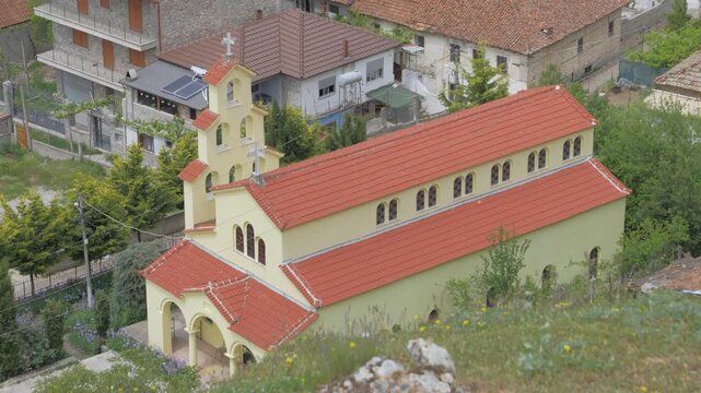 High angle view of the Church of Saint Barbara in Lin, a village on Lake Ohrid in southeast Albania, with its bell tower, red tiled roof and arched porch among homes.