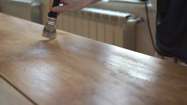 Home renovation: applying protective varnish to a wooden table with a brush