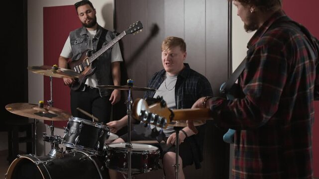 Caucasian young men rehearsing in music studio playing drums and electric guitars. Footage suitable for music school commercials, creative youth campaigns, and band promotions