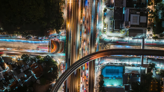 Aerial view of a busy highway intersection at night in Jakarta, Indonesia, featuring vibrant light trails from moving vehicles and urban infrastructure.