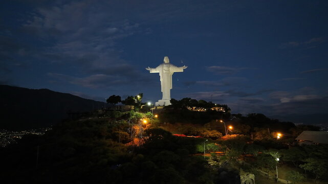 Aerial view of Christ of the Concord Monument illuminated at night atop San Pedro Hill, surrounded by trees and city lights Cochabamba, Departamento de Cocha, Bolivia.