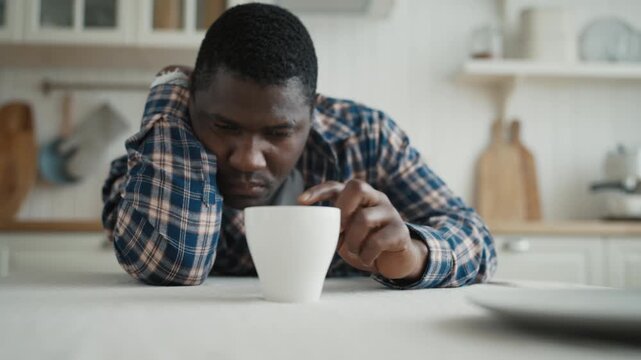 Portrait of unhappy black man at kitchen in morning, person looking at cup. Loneliness and depression, stay alone at home and suffer of divorce or job loss, adult male person missing and feeling sad